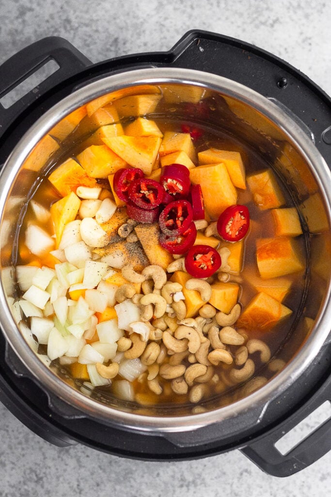 Instant Pot filled with dived pumpkin, onions, cashews, peppers, and broth.