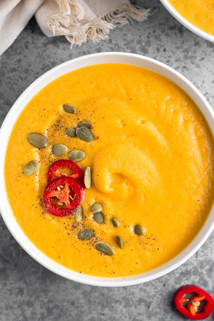 Overhead shot of vegan pumpkin soup garnished with pumpkin seeds, chili pepper, and pepper.