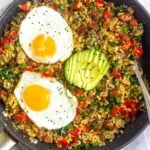 Large saute pan filled with whole30 and paleo breakfast fried rice topped with two fried eggs, sliced avocado, and sesame seeds