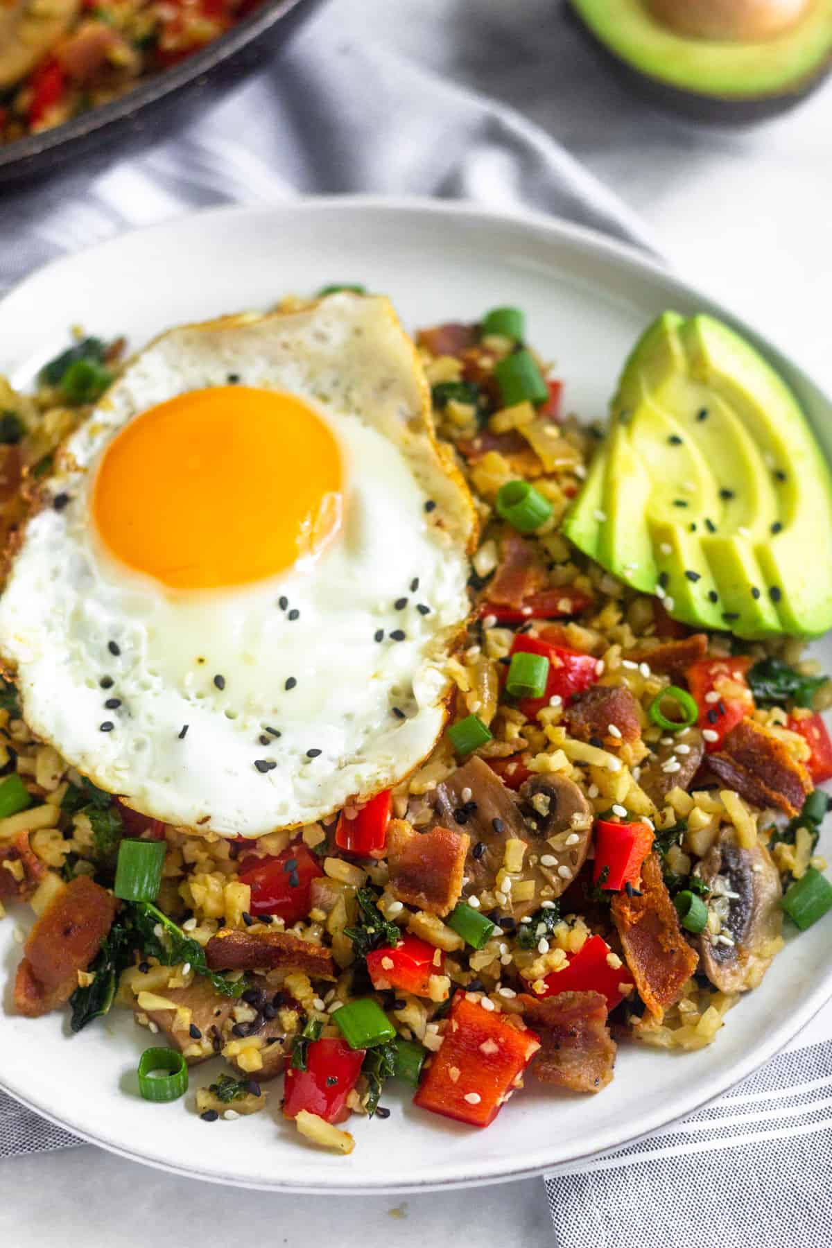 Large white plate filled with whole30 and paleo breakfast fried rice topped with a fried egg, avocado slices, and sesame seeds