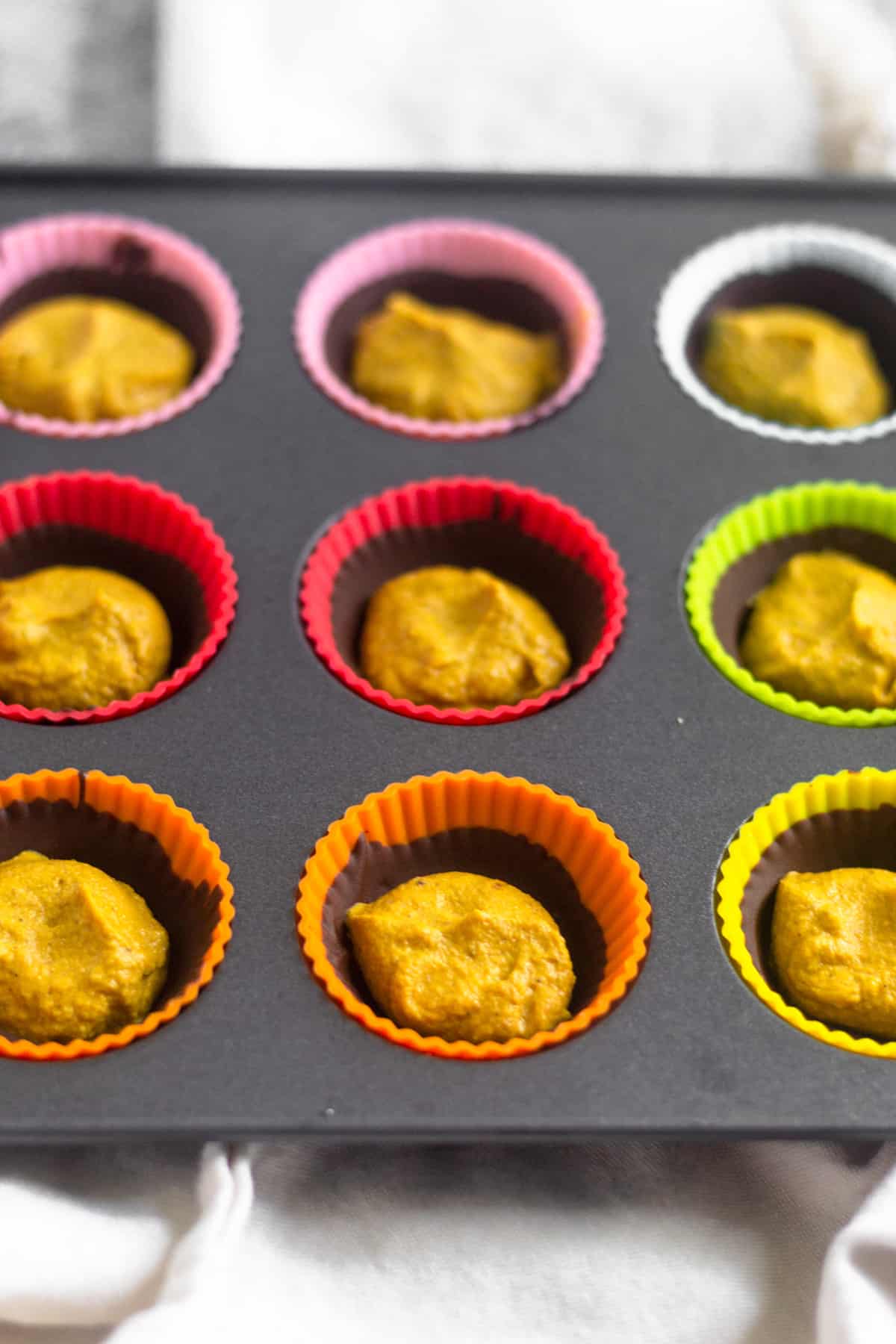 Mini muffin tin tray with half made pumpkin pie chocolate cups in them. There is a shell of chocolate and then a scoop of pumpkin pie butter in them.