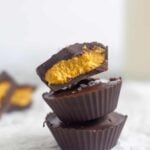 Close up of three pumpkin pie chocolate cups stacked on top of each other. The top one is cut in half. Behind them are more cut open chocolate ups and a jar of milk.