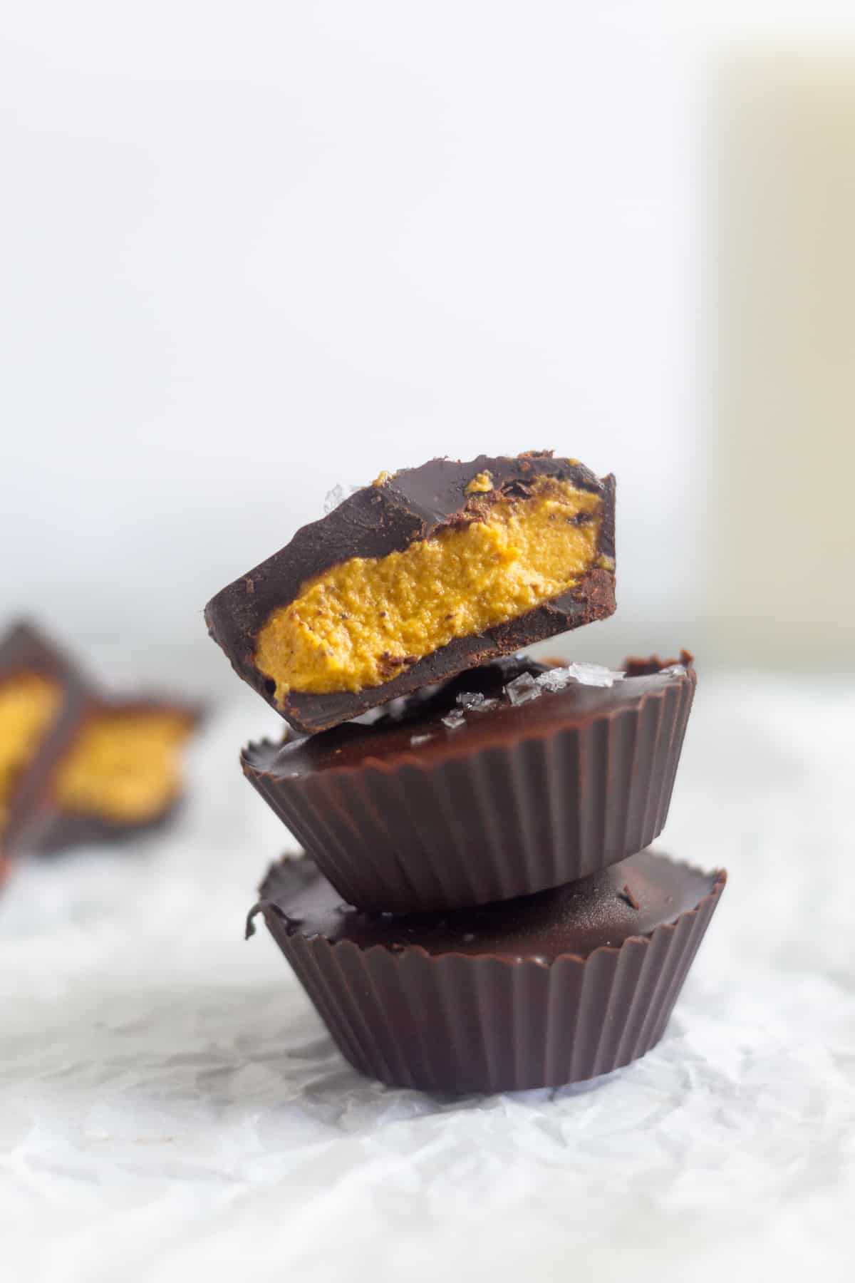 Close up of three pumpkin pie chocolate cups stacked on top of each other. The top one is cut in half. Behind them are more cut open chocolate ups and a jar of milk.