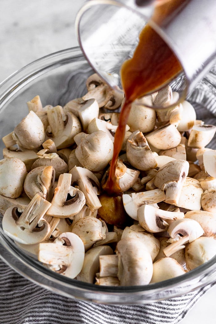 Bowl of mushrooms that have been halved or quarter with a balsamic dressing being poured on them.