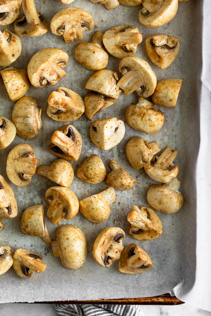 Baking sheet filled with halved and quartered mushrooms topped with balsamic vinegar.