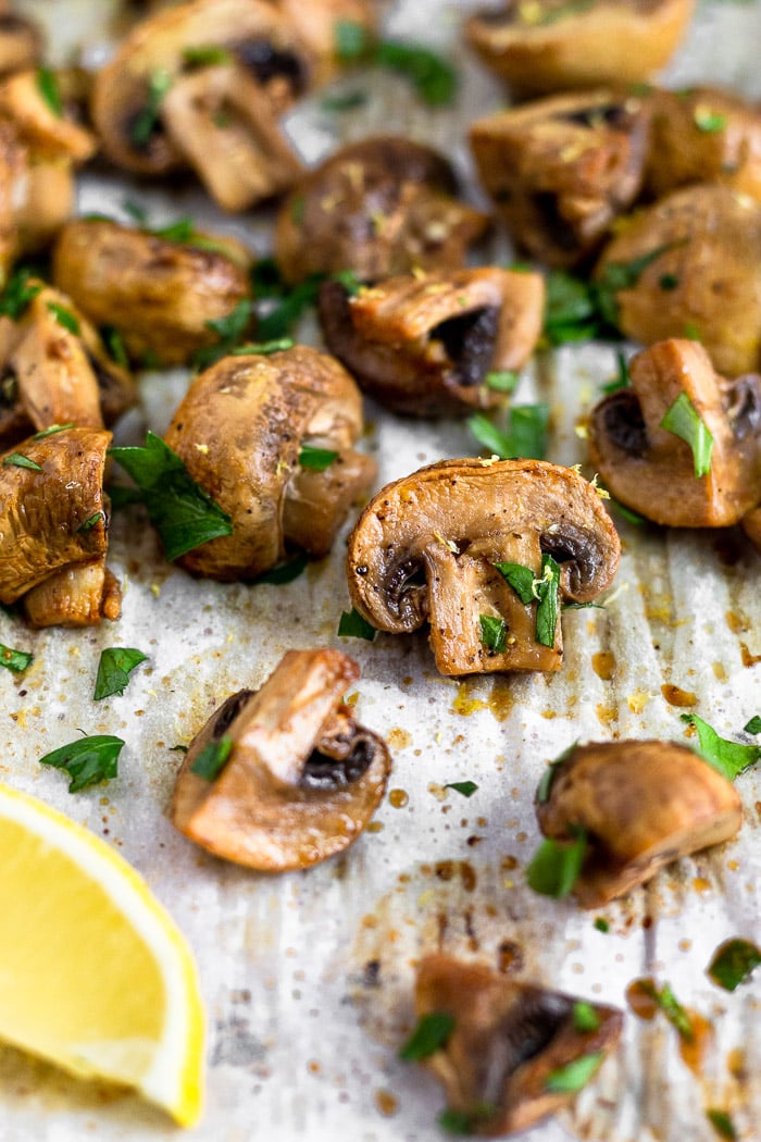 Baking sheet filled with balsamic roasted mushrooms topped with fresh parsley and a lemon wedge in the corner.