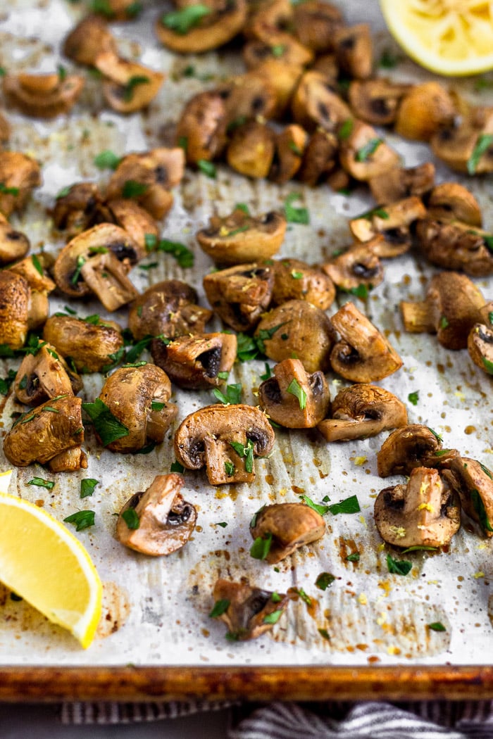 Baking sheet filled with roasted mushrooms topped with fresh parsley with a lemon wedge in the corner.