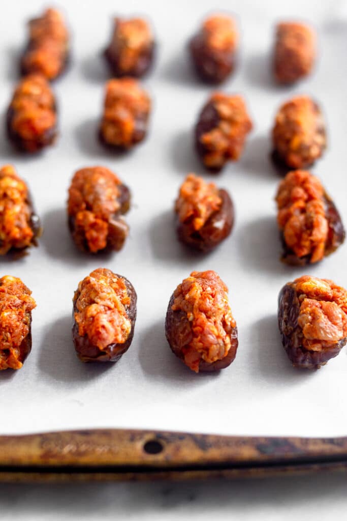 Dates stuffed with chorizo on a baking sheet lined with parchment paper before they are cooked.