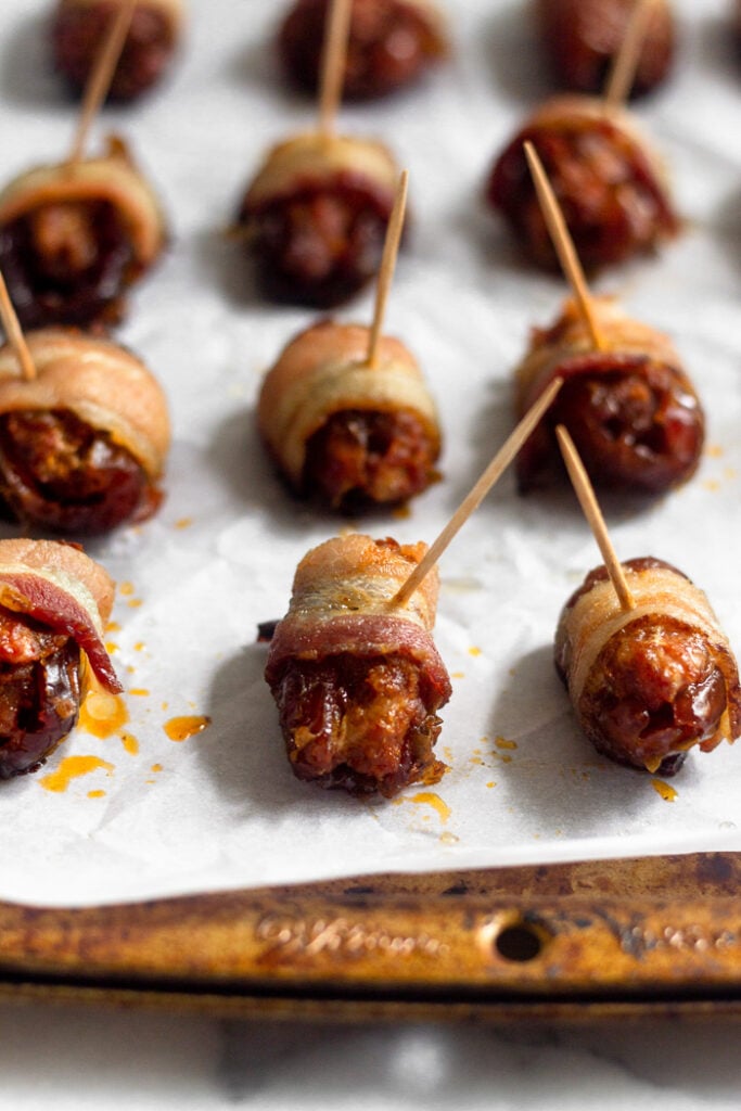 Baking sheet with cooked bacon wrapped dates on them.