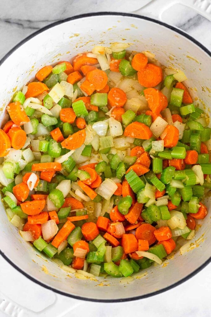 Large white dutch oven filled with diced sautéed onions, carrots, and celery.