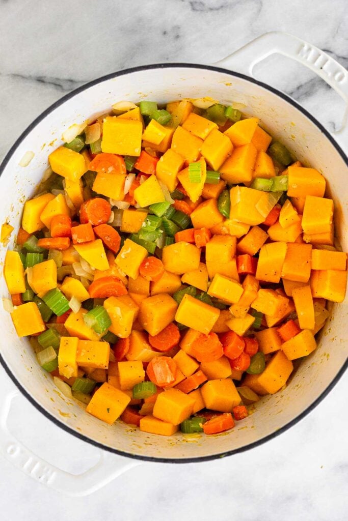 Large white dutch oven filled with a mix of sautéed veggies and cubed butternut squash.