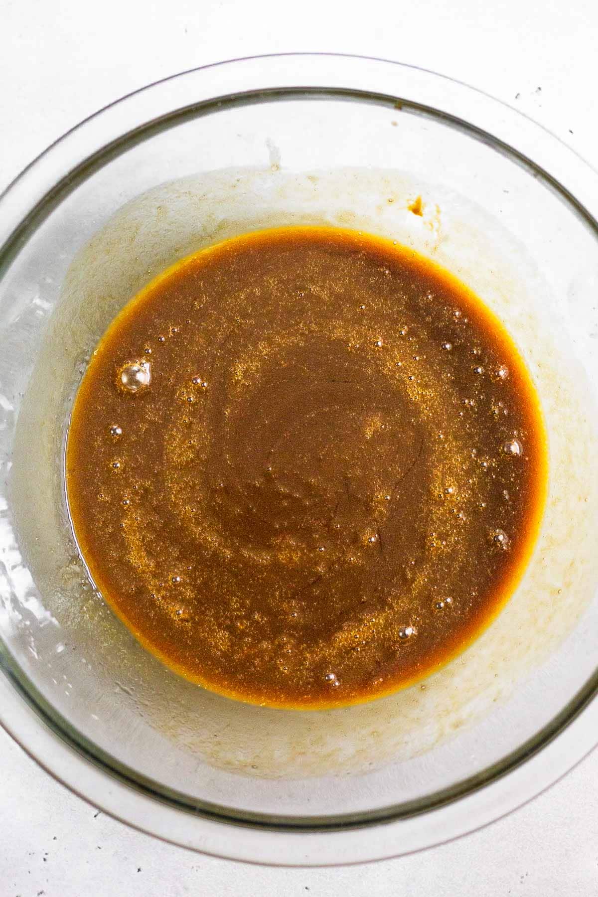 A glass bowl of butter, eggs, and molasses that has been whisked together.