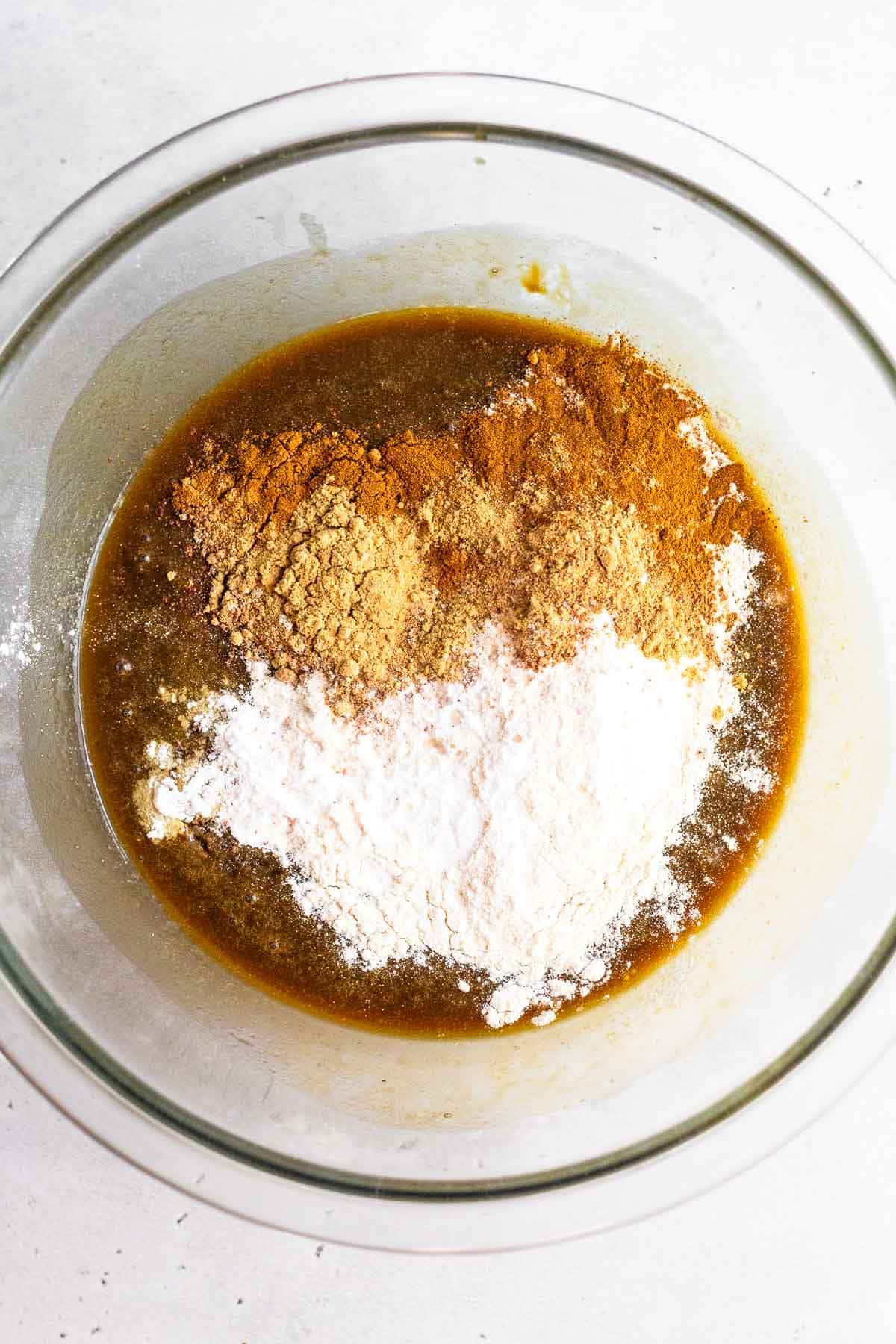 A glass bowl of batter with flour and spices on top of it.