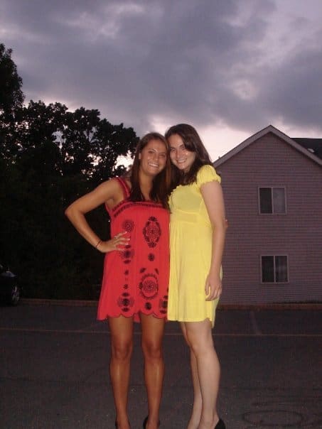 Two girls in dresses outside in a parking lot. One in a red dress, one in a yellow dress.