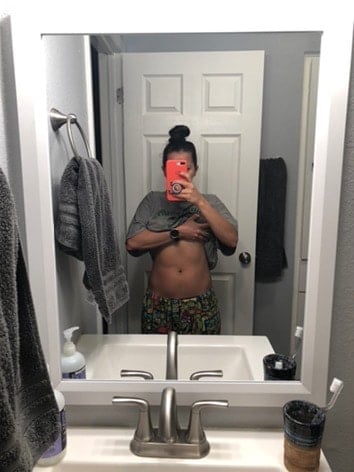 Girl in the bathroom lifting up her shirt to show her stomach