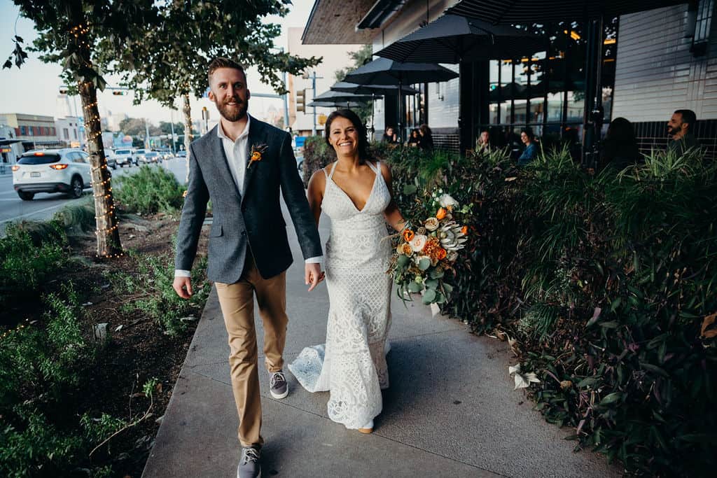 Married couple with the bride holding her bouquet walking down the street on a sidewalk