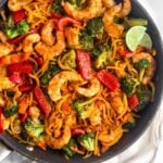 A large sauté pan with Whole30 Shrimp & Butternut Squash Noodles with Curry Peanut Sauce garnished with two lime wedges