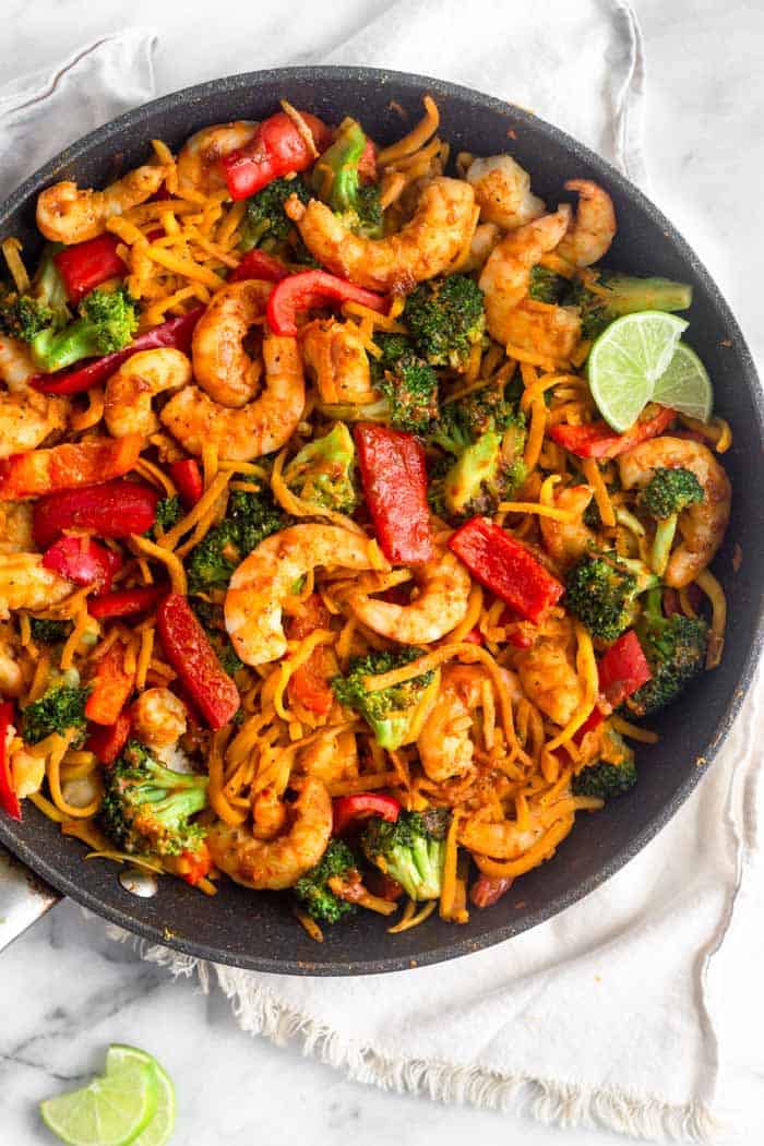 A large sauté pan with Whole30 Shrimp & Butternut Squash Noodles with Curry Peanut Sauce garnished with two lime wedges
