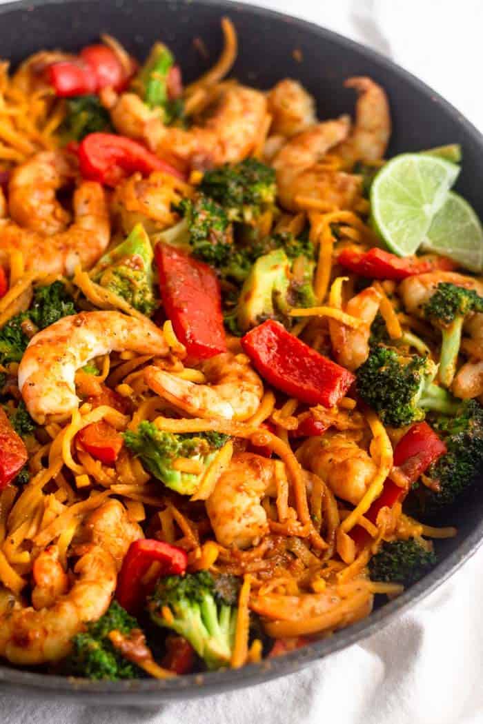 Close up of a pan of Whole30 Shrimp & Butternut Squash Noodles with Curry Peanut Sauce. Two lime wedges are on the right side garnishing it.