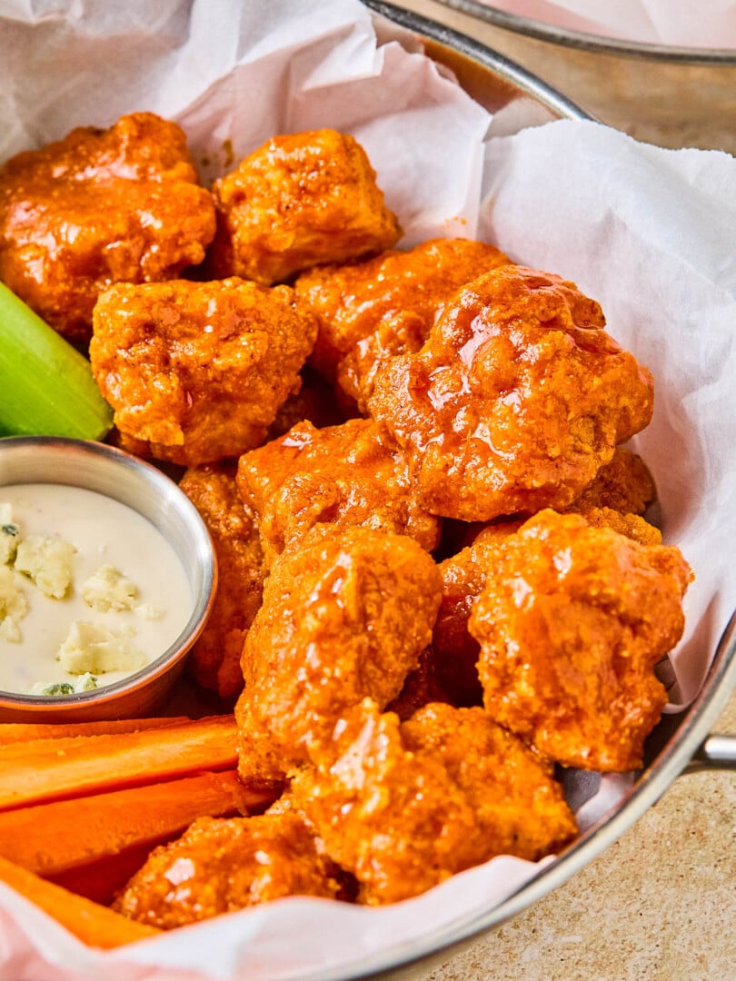 Air fryer boneless buffalo wings in a basket with carrot sticks, celery sticks, and a small ramekin of blue cheese dressing.