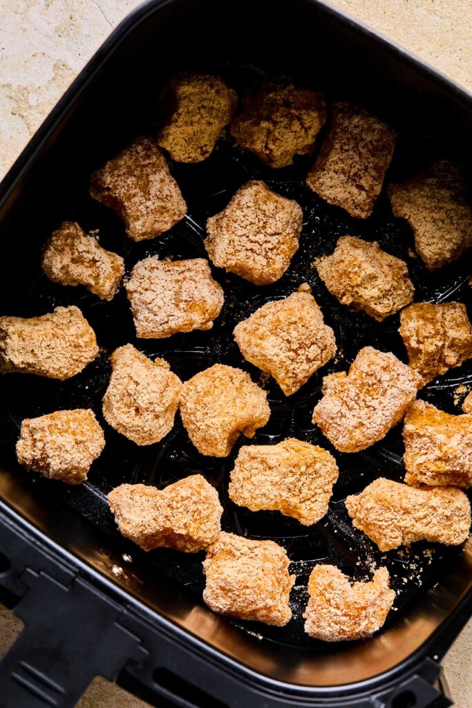 Breaded chicken pieces in an air fryer basket before they are cooked.