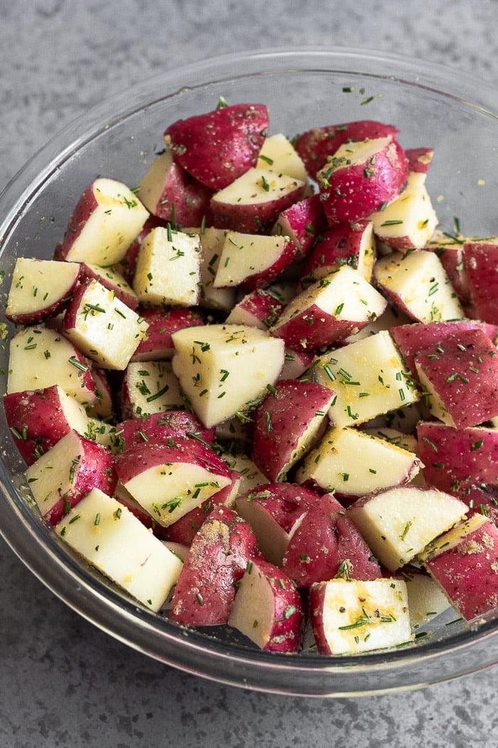 Bowl of diced red potatoes coated in oil, spices, and rosemary.