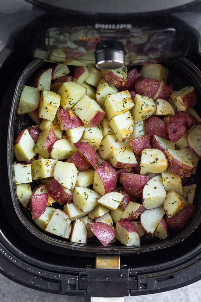 Halfway cooked diced red potatoes in an air fryer basket.