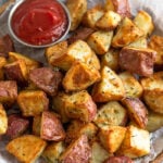 Plate of crispy rosemary garlic air fryer potatoes with a small ramekin of ketchup next to them.