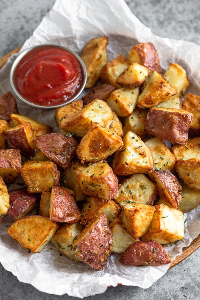Plate of crispy rosemary garlic air fryer potatoes with a small ramekin of ketchup next to them.