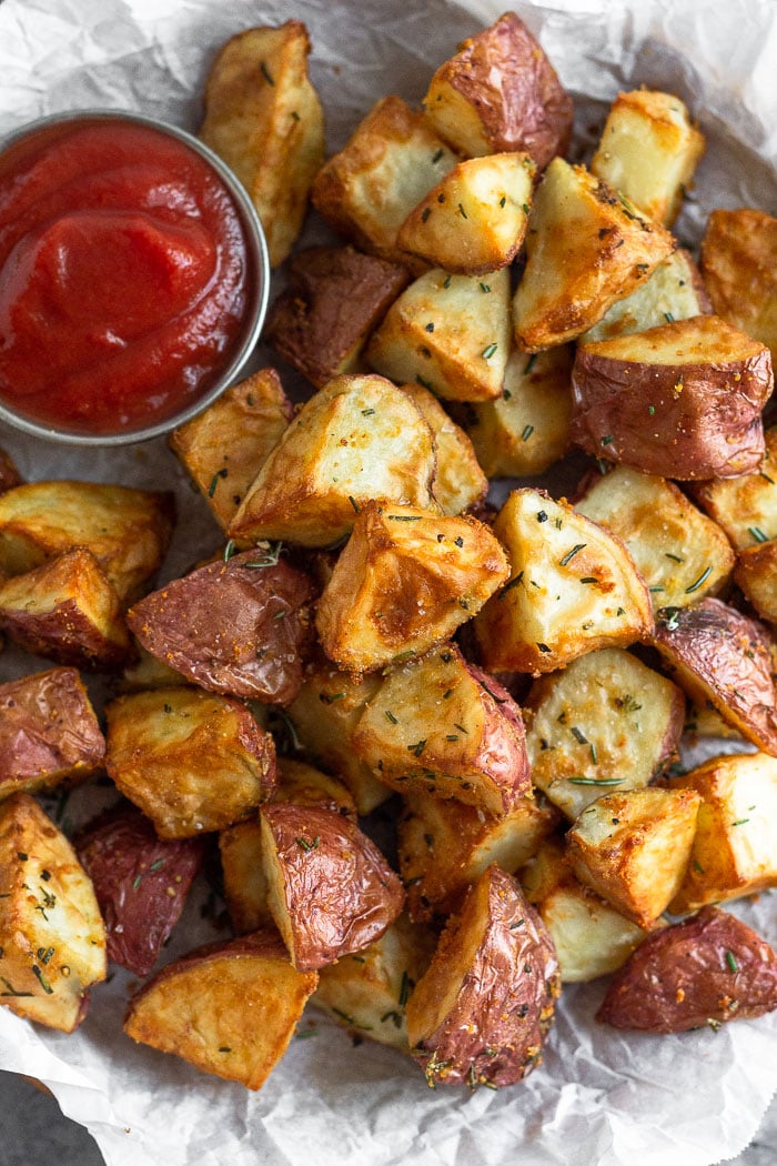 Crispy rosemary garlic potatoes on a plate with a ramekin of ketchup next to them.