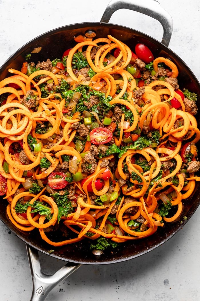 Overhead shot of a pan filled with cooked ground beef and veggies with sweet potato noodles mixed in.