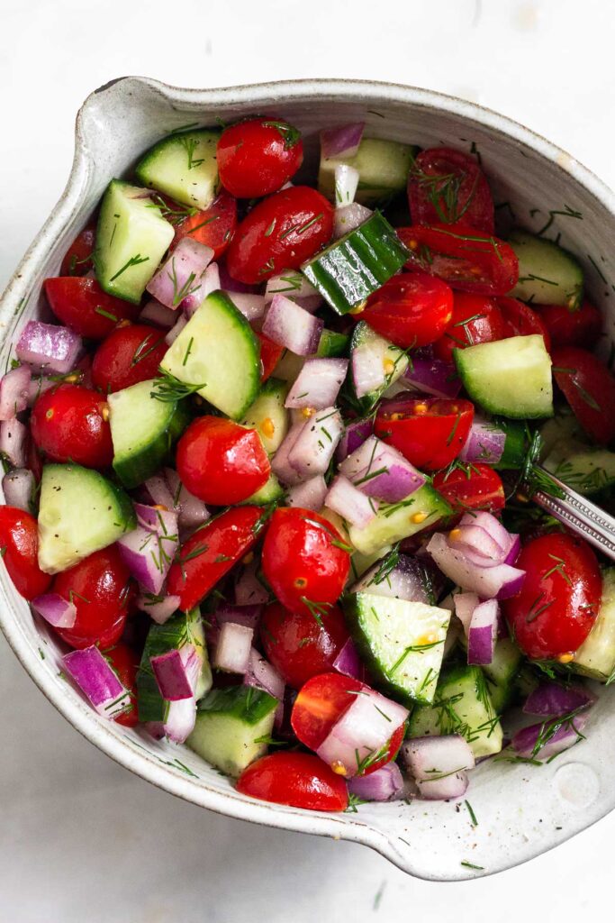 A bowl filled with diced tomato, diced cucumber, diced red onion, herbs, and spices all mixed together.