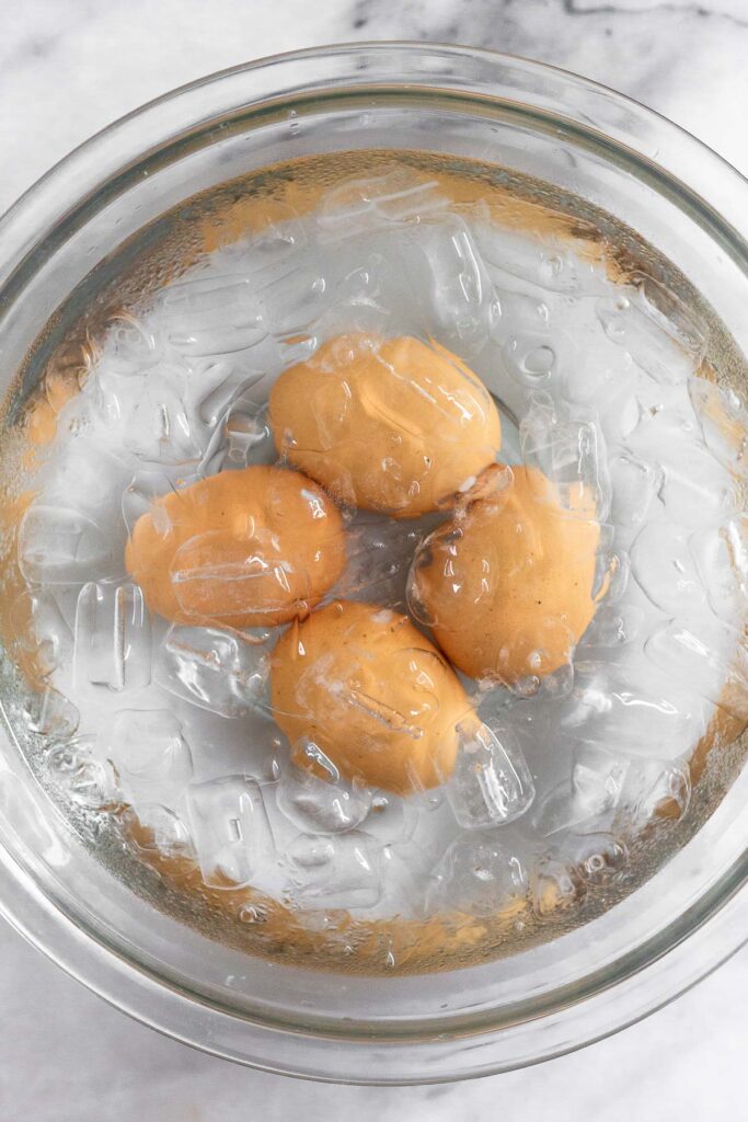 A glass dish filled with water and ice cubes with four eggs in it.