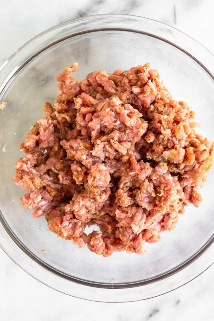 Ground pork mixed with spices in a glass bowl.