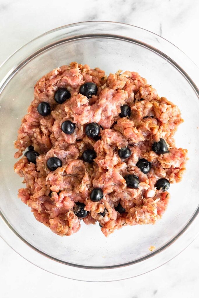 Ground pork, spices, and fresh blueberries all mixed together in a large glass bowl.