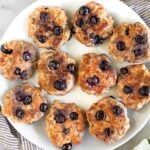 A white plate of blueberry breakfast sausage patties. They plate is sitting on a kitchen towel and next to it is a bowl of blueberries.