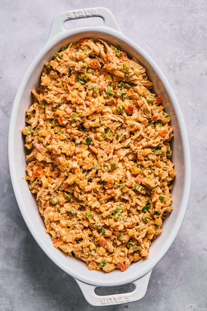 A mixture of shredded chicken and veggies in a creamy red sauce in a white au gratin dish before it is baked.