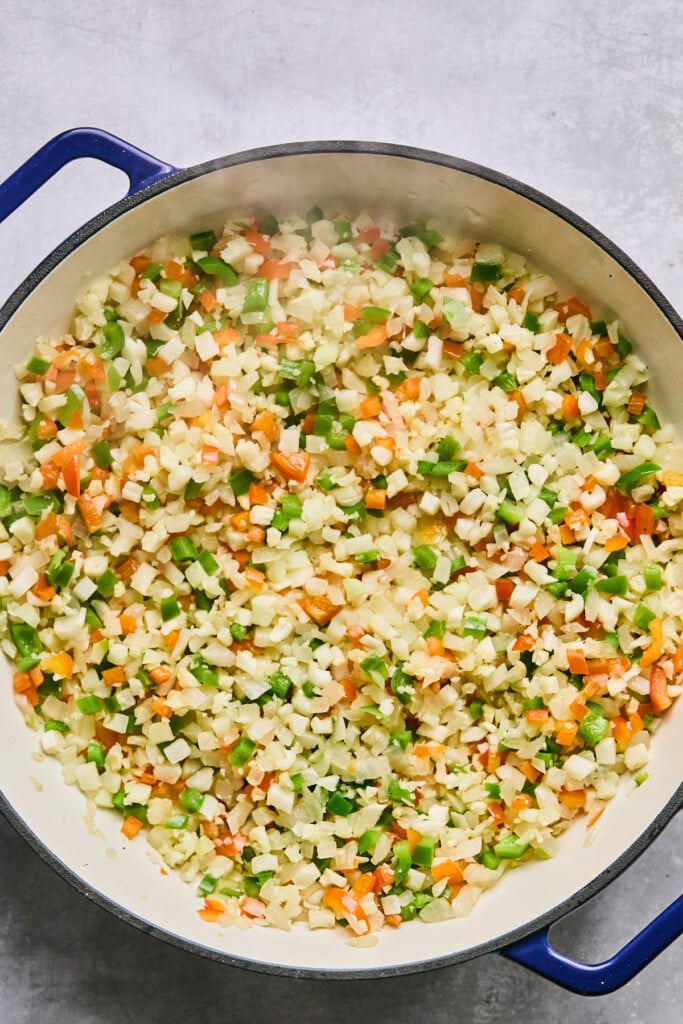 Large enameled pan filled with sautéed onions, peppers, and cauliflower rice.