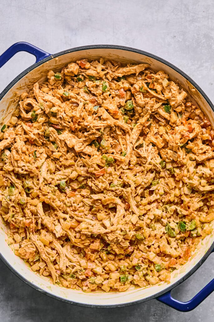 Large enameled pan filled with a mixture of shredded chicken and veggies in a creamy red sauce.