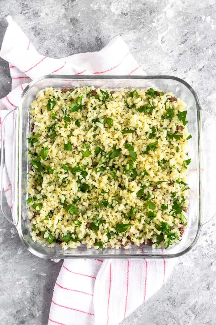 Glass dish filled with taco ground beef and a layer of cilantro lime cauliflower rice on top.