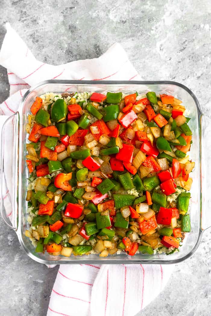 Glass dish filled with taco ground beef, cilantro lime cauliflower rice on top, and a layer of sautéed fajita veggies on top.