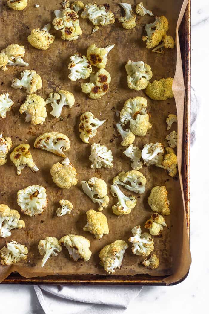 A baking sheet with parchment paper and roasted cauliflower on it.