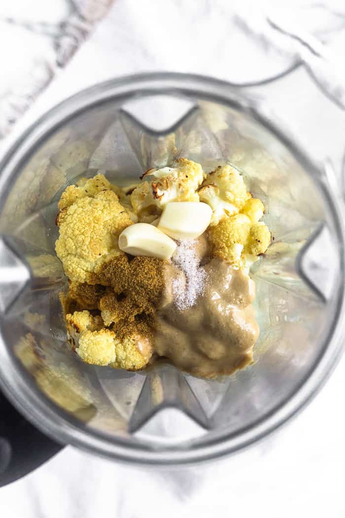 A blender filled with the ingredients of paleo cauliflower hummus - roasted cauliflower, tahini, garlic, cumin, and lemon juice.