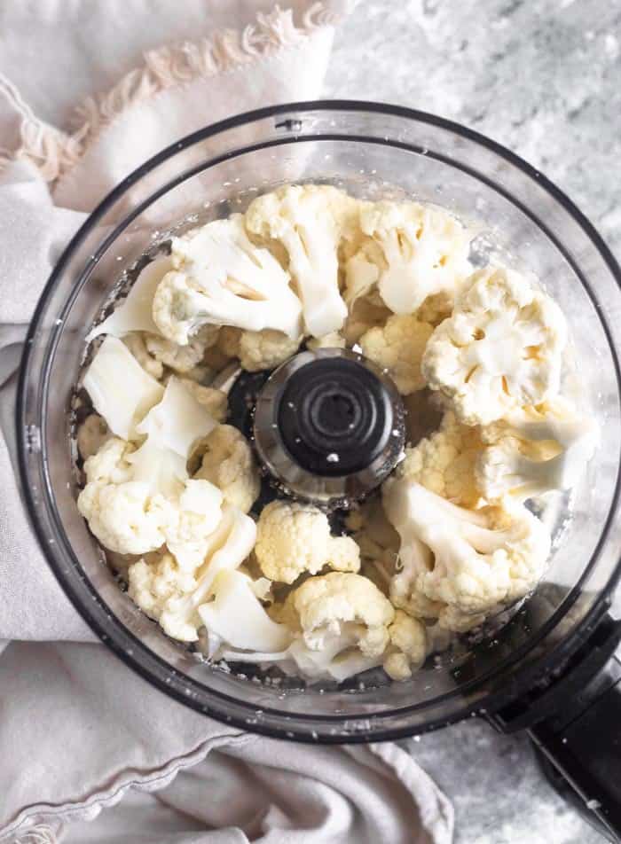 Cauliflower florets in a bowl of a food processor.