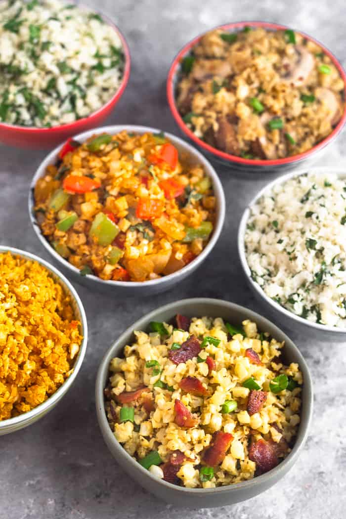 Six different bowls of cauliflower rice on a grey surface. Picture is shot at a 45 degree angle where the front is in focus and the back is blurred.