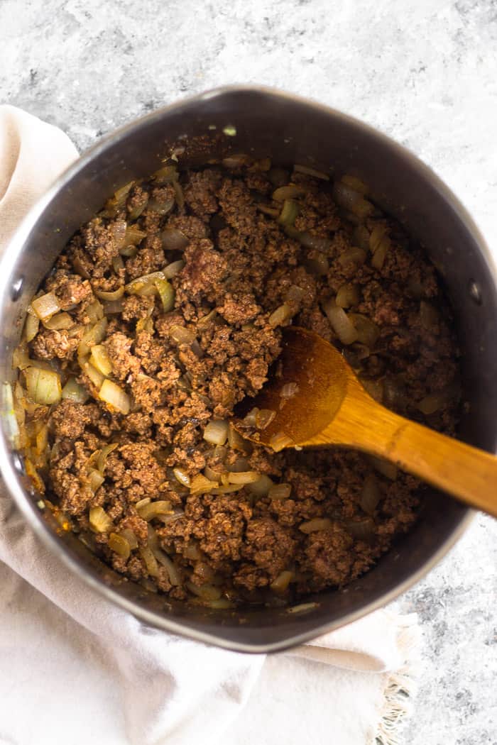 Large stock pot filled with sautéed ground beef and onions. A wooden spoon is in the pot.