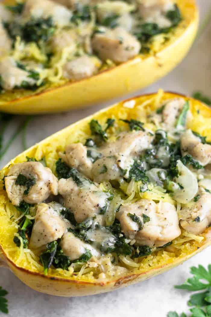 Spaghetti squash boat stuffed with chicken Caesar salad. Another stuffed spaghetti squash is behind it and a few sprigs of parsley are around it.