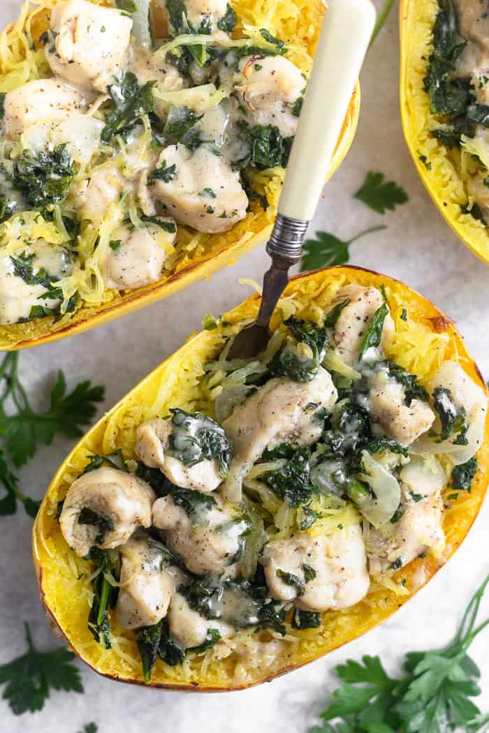 Overhead shot of 2 chicken caesar spaghetti squash boats with parsley leafs around them. A fork is stuck in one of them.