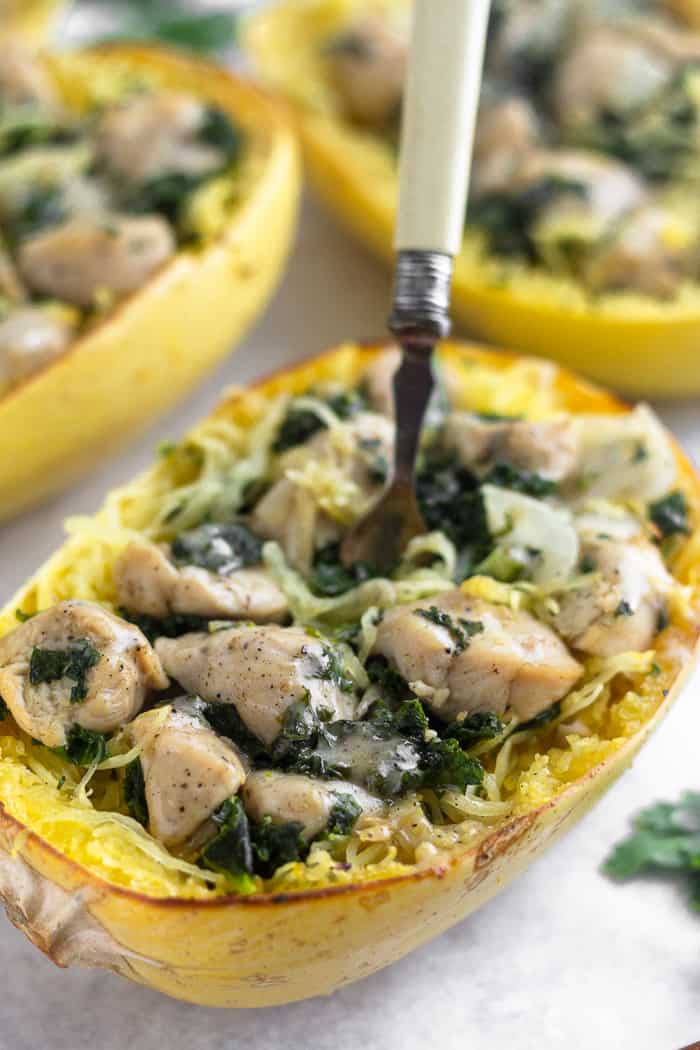 A sheet filled with chicken caesar spaghetti squash boats with parsley laying next to them. One boat has a fork sticking out of it.