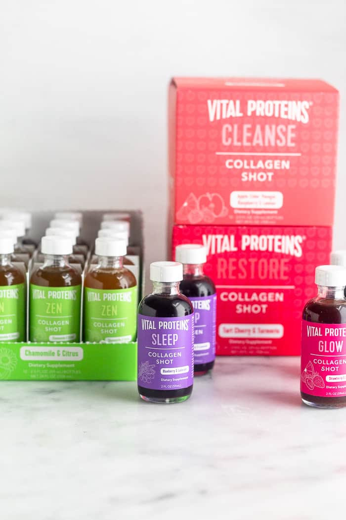 Three boxes full of collagen shots, one of them being open so you can see inside of it. Three more bottles are sitting around the boxes. There are five different flavors in total.